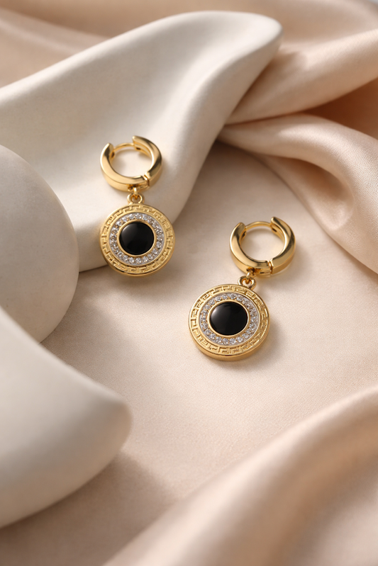 Gold hoop earrings with black gemstones on a beige fabric background