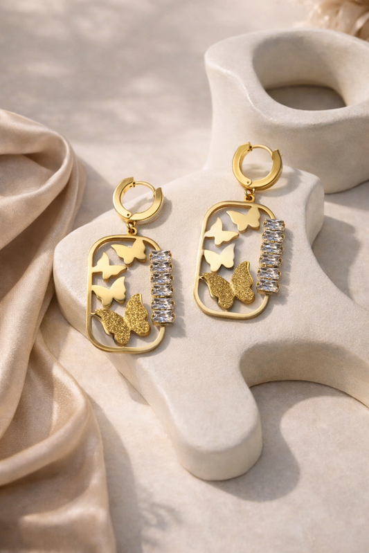 Gold butterfly earrings with crystal accents on a beige fabric background