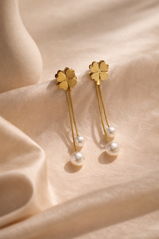 Gold earrings with clover-shaped tops and pearl drops on a beige fabric background