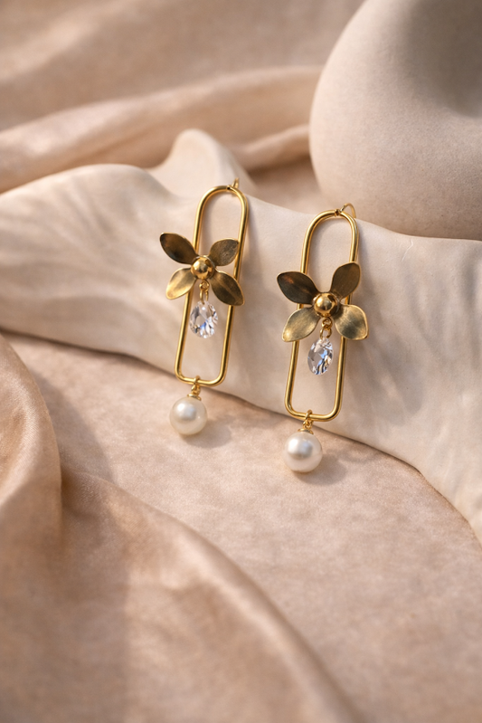 Gold earrings with floral designs and pearls on a beige fabric background