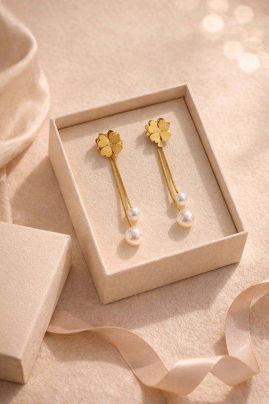 Gold earrings with pearl drops in a beige box on a soft pink background