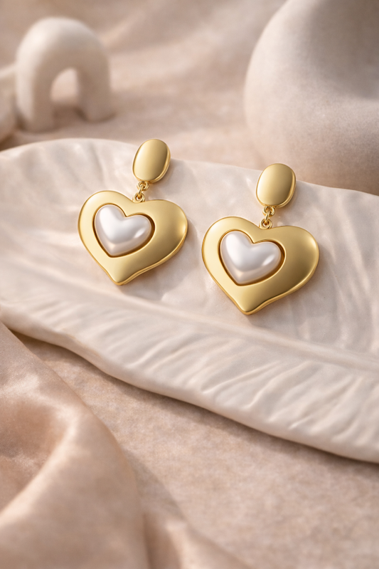 Gold heart-shaped earrings with a pearl center on a soft beige fabric background