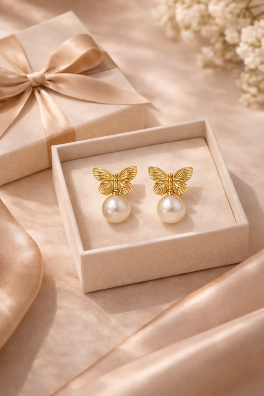 Gold butterfly earrings with pearl centers in a box on a soft pink background