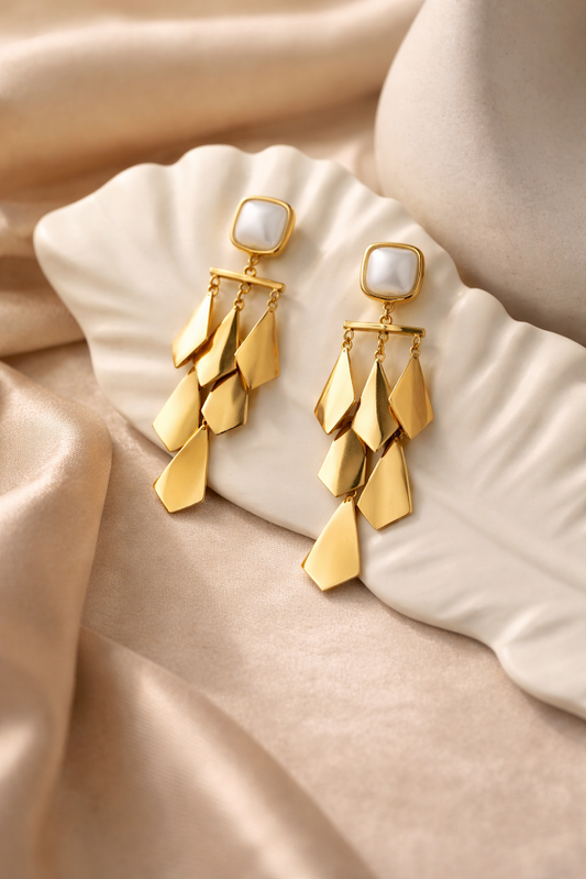 Gold earrings with pearl accents on a beige fabric background
