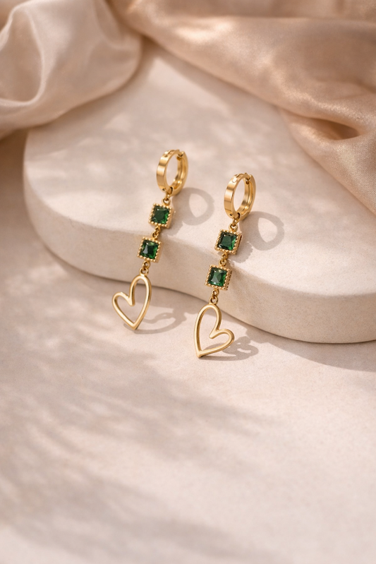Gold earrings with heart and gemstone details on a beige fabric background