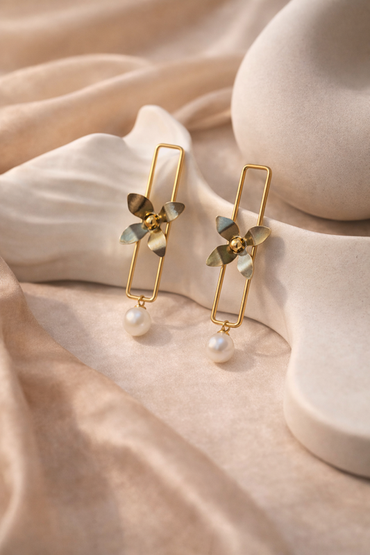 Gold earrings with leaf-like designs and pearl beads on a beige fabric background