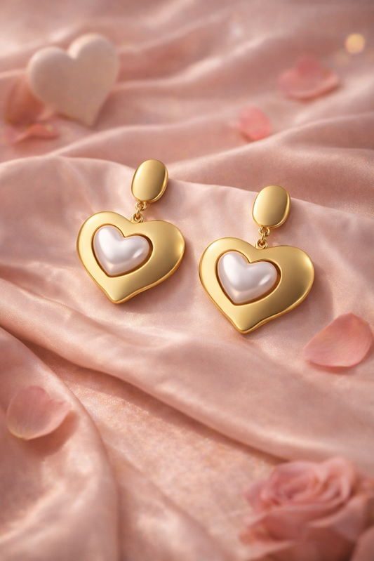 Heart-shaped earrings with gold and pearl finish on a soft pink fabric background