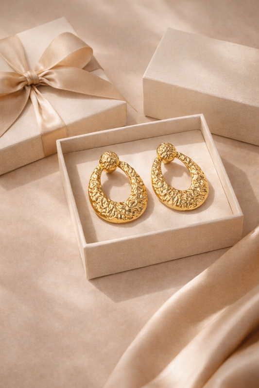 Gold earrings in a box with a matching gift box on a beige surface