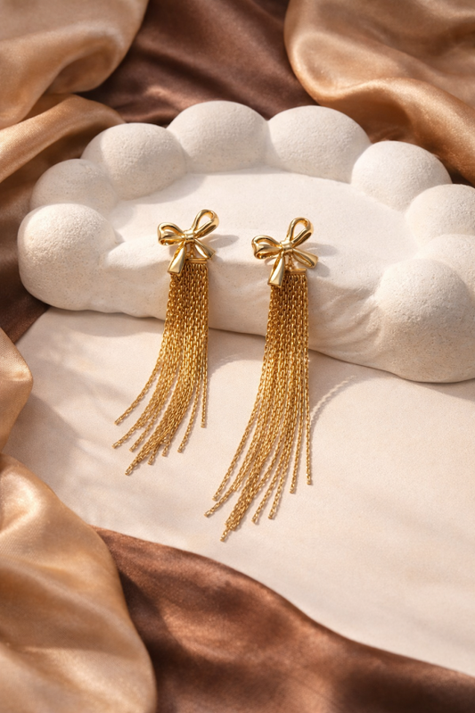 Gold tassel earrings on a white stone surface with brown fabric background