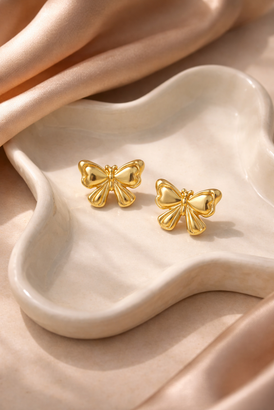 Gold butterfly earrings on a beige ceramic dish