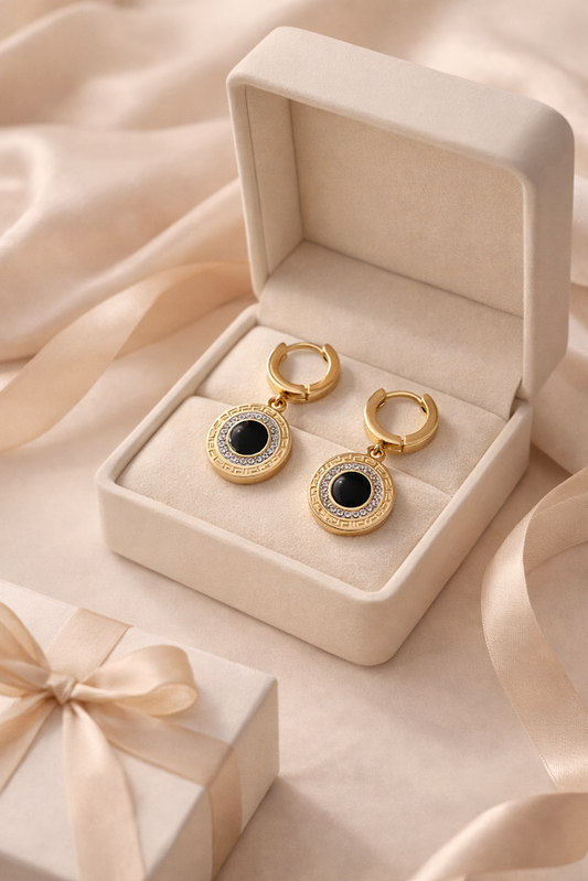 Gold earrings with black stones in a beige jewelry box on a soft pink fabric background