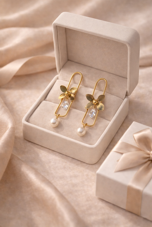Gold earrings with pearl accents in a jewelry box on a soft beige fabric background