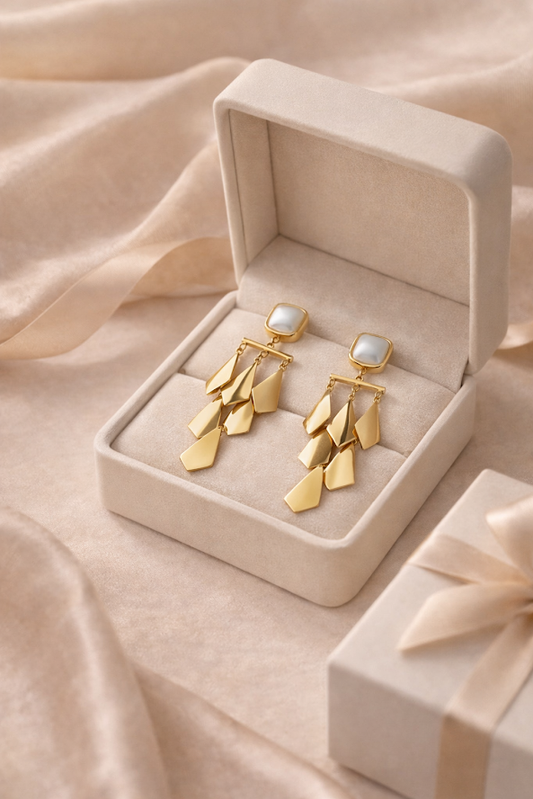 Gold earrings with pearl accents in a jewelry box on a soft beige fabric background
