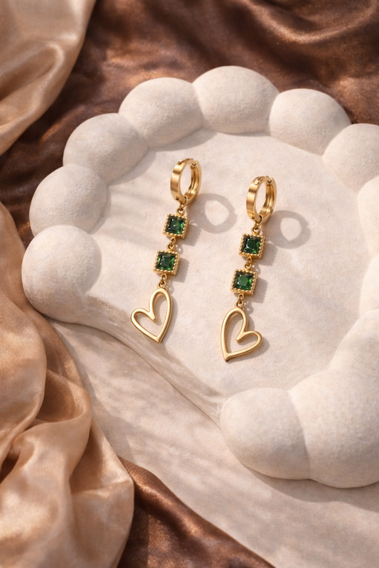 Gold earrings with green gemstones on a white stone surface