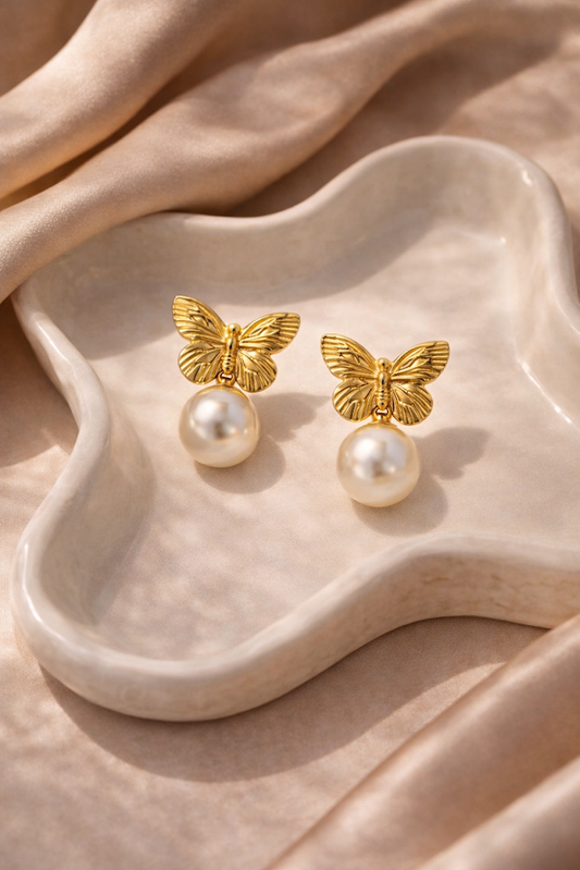 Gold butterfly earrings with pearl centers on a beige dish.