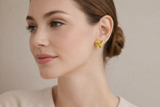 Woman wearing gold heart-shaped earrings against a neutral background